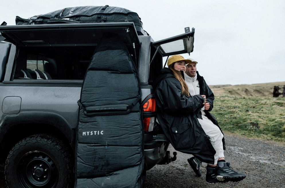 Woman in a changing robe sitting in the boot of a 4x4 loaded with board bags on a coastal track