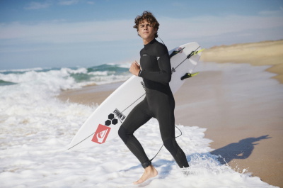 Surfista in muta Quiksilver che cammina in spiaggia con la tavola