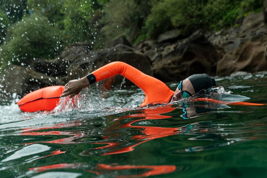 Nageur en eau libre en combinaison à manches orange fluo, en crawl derrière une bouée de nage orange