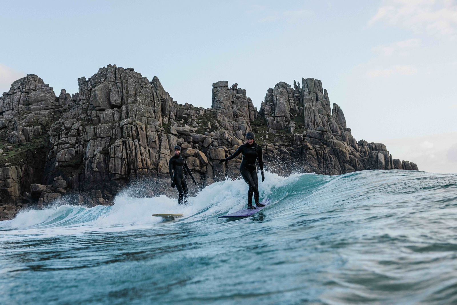 Surfeur sur une petite vague bien formée au pied de hautes falaises de granit