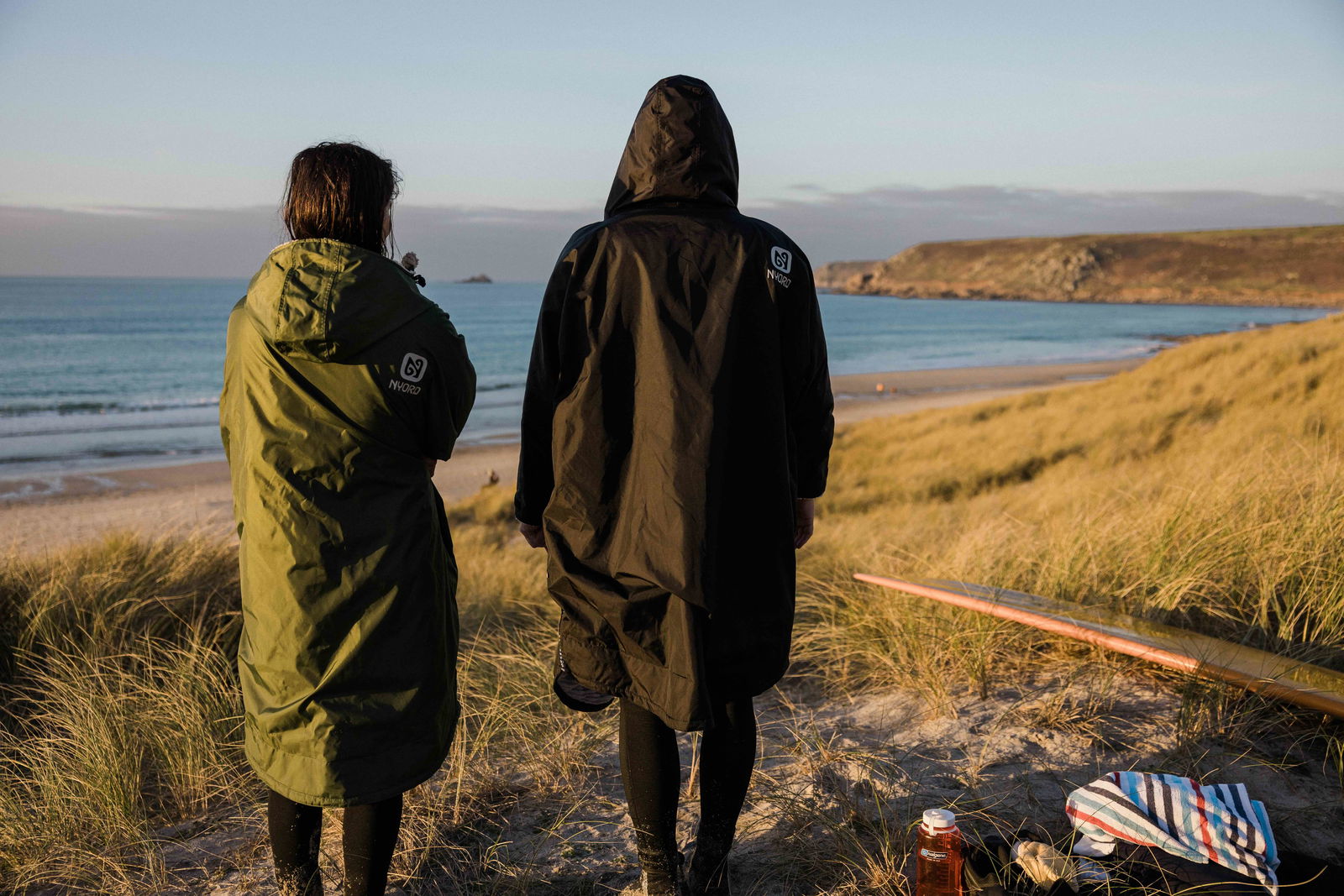 Deux personnes en longs ponchos de change à capuche regardant la plage au coucher du soleil