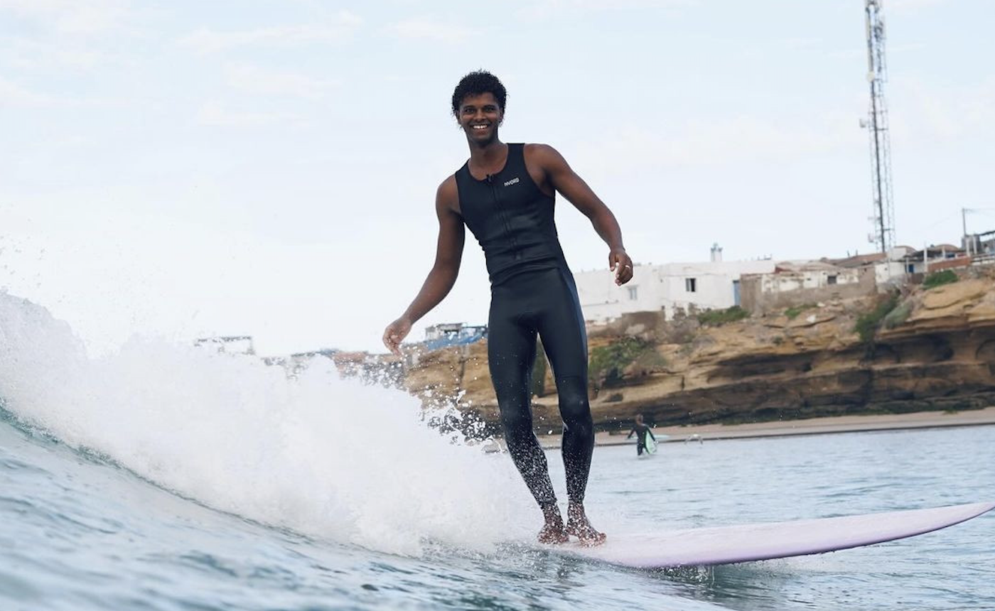 Surfeur en combinaison noire sans manches glissant dans la mousse sur un longboard