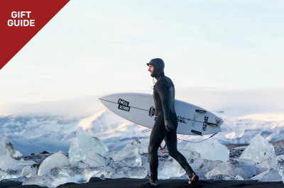 Surfeur en combinaison et cagoule portant sa planche dans les dunes