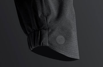 Close-up of the elasticated hem and cuff of a dark technical jacket on a black studio background