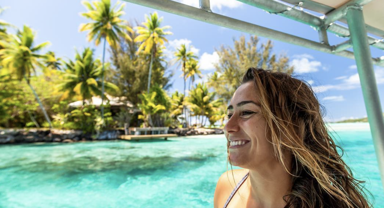 Woman laughing aboard a boat with palm-fringed islets and turquoise lagoon behind her