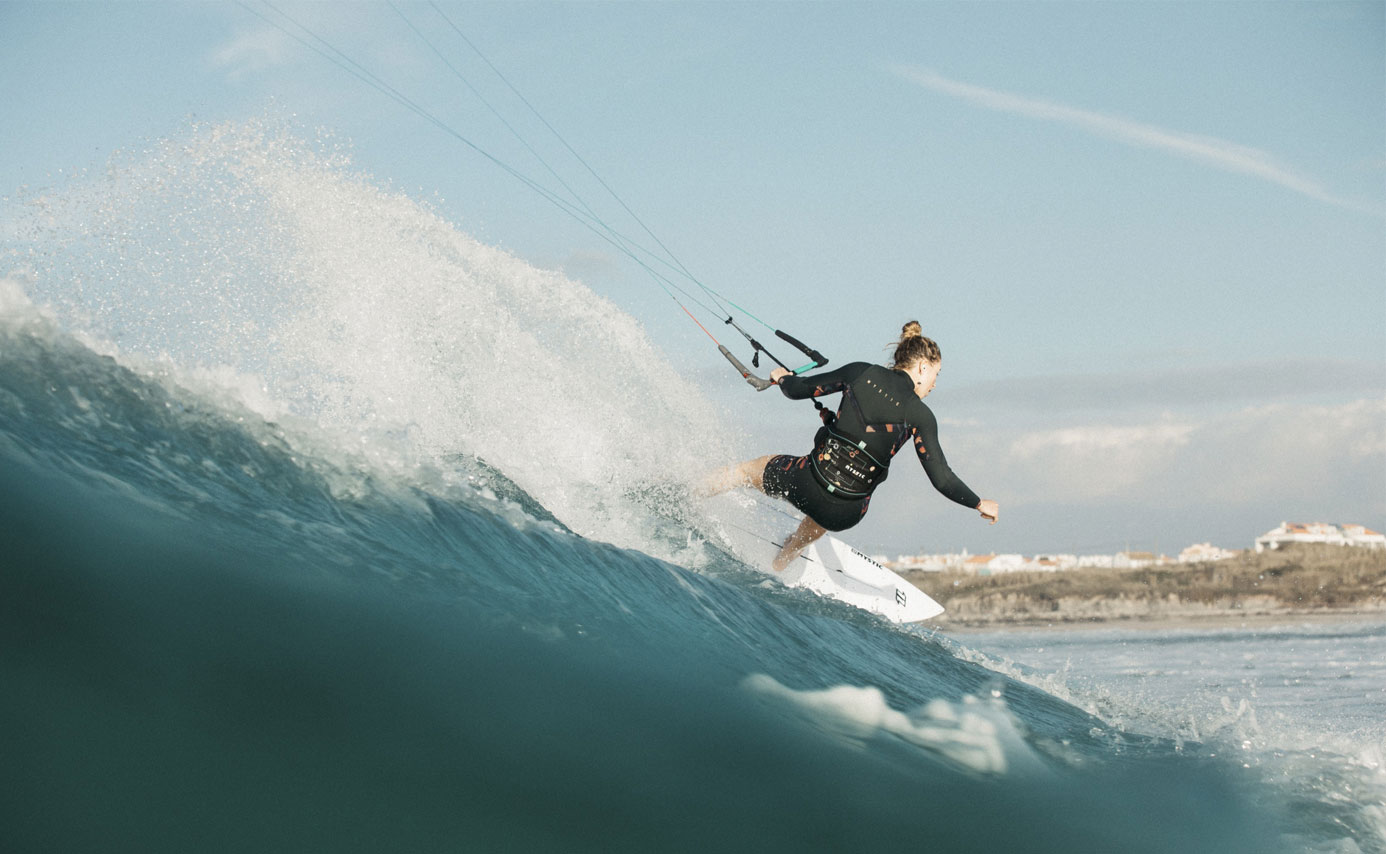 Kitesurfer carving down the face of a breaking wave with the kite lines overhead