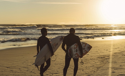 Surfeurs en combinaison en contre-jour devant un coucher de soleil